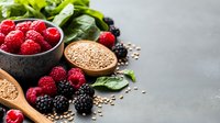 Fresh raspberries and blackberries with flax seeds and green spinach leaves on dark concrete background, healthy superfood ingredients for breakfast.