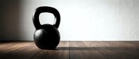 Black kettlebell with handle on wooden floor against white wall, suitable for fitness, gym, and workout design projects.
