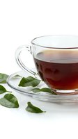 Clear glass teacup with saucer filled with dark tea surrounded by fresh green tea leaves on white background isolated for design use.