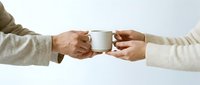 Two hands passing a white ceramic coffee mug, symbolizing sharing, care, and connection in everyday moments of warmth and hospitality.