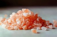 Pink Himalayan salt crystals in macro view on light surface, showing natural mineral texture and varying shades of pink and orange hues.