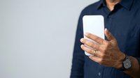 Man in dark navy shirt holding blank white mobile device with both hands against neutral background, suitable for app promotion, technology marketing, and digital communication concepts.