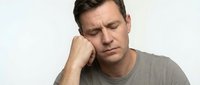 Middle-aged Caucasian man experiencing headache or stress, holding head with hand while sitting against white background for health and wellness concepts.