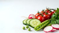 Fresh organic vegetables including cherry tomatoes, cucumber slices, peas, radishes and parsley arranged on white background for healthy cooking and nutrition.