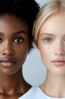 Close-up portrait of two diverse young women with contrasting skin tones and features, showcasing natural beauty and racial diversity against light background.