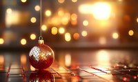 Red Christmas ornament on wooden surface with warm golden bokeh lights creating festive holiday atmosphere.