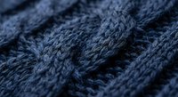 Close-up macro shot of dark blue knitted wool fabric showing detailed cable knit texture and fiber structure for textile and fashion design projects.