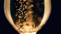 Champagne bubbles rising in a glass against dark background, golden effervescent liquid with sparkling particles, celebration and luxury beverage concept.