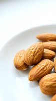 Whole almonds arranged on white plate, showcasing natural texture and rich brown color, suitable for food photography, nutrition content, healthy snacking, and culinary design projects.