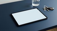Black tablet with blank white screen on modern blue desk workspace with glass of water and keys for digital mockup presentations.