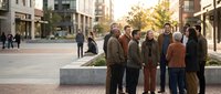 Diverse group of senior friends standing together on urban plaza during golden hour sunset, smiling and enjoying retirement lifestyle in modern city center.