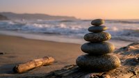 Zen stone stack on sandy beach at sunset with ocean waves creating peaceful meditation and balance concept for wellness and mindfulness practices.