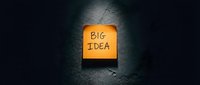 Big idea concept with orange sticky note on dark textured wall surface, representing innovation, creativity, and business brainstorming solutions.