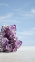 Purple amethyst crystal cluster on white surface against soft blue sky with wispy clouds for wellness and spiritual healing concepts.