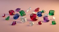 Collection of colorful precious gemstones including diamonds, rubies, emeralds and sapphires scattered on pink surface for jewelry design and luxury concepts.