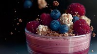 Fresh raspberry and blueberry smoothie bowl topped with granola crumbs and berries floating against dark background, healthy breakfast concept.