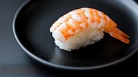 Fresh shrimp nigiri sushi on black ceramic plate against dark background, traditional Japanese cuisine with white rice and orange prawn, macro food photography.