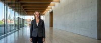 Professional woman in business attire standing in modern office corridor with concrete walls and wooden ceiling, suitable for corporate and workplace concepts.