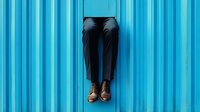 Person in dark jeans and brown leather boots standing against vibrant blue corrugated metal wall background for urban fashion and lifestyle concepts.