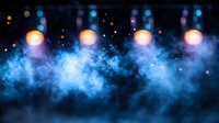 Stage lights illuminate dramatic blue smoke effects creating atmospheric concert venue backdrop for live entertainment performances.