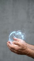 Cupped hands holding glowing digital globe with sparkling particles against concrete wall background for technology and innovation concepts.