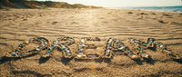 Word relax written with colorful shells and pebbles on golden sandy beach at sunset, warm sunlight glowing over ocean shore.