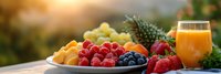 Fresh tropical fruits and berries with orange juice glass on wooden table during golden hour sunset creating healthy breakfast scene.