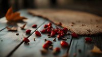 Red berries scattered on rustic wooden table with burlap fabric and autumn leaves creating moody atmospheric composition for food styling and seasonal decor.