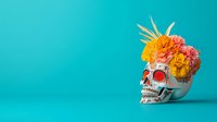 Decorative skull with bright marigold flowers and tropical leaves crown against turquoise background, celebrating Day of Dead Mexican tradition and culture.