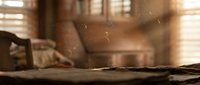Dust particles floating in warm sunlight streaming through window blinds in cozy living room interior with soft bokeh background.