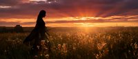 Woman in silhouette walking through wildflower field at golden hour sunset, dramatic sky with warm orange and red tones, rural landscape photography for nature and lifestyle use.