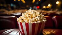 Fresh popcorn in classic red striped container with blurred cinema seats background, capturing movie theater ambiance and entertainment atmosphere.