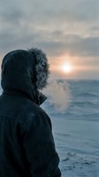 Person wearing dark winter coat with fur-lined hood gazing at ocean horizon during sunset. Solitude and contemplation by the sea.