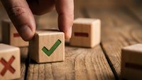 Hand placing wooden block with green checkmark among blocks with red X and minus signs on rustic table, symbolizing approval and decision making.