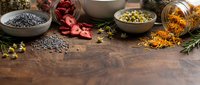 Aromatic spices and herbs scattered on rustic wooden table with bowls containing colorful seasonings for culinary cooking and food preparation.