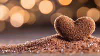 Heart shape made from brown sugar or coffee grounds on blurred bokeh background with warm golden lights, romantic macro photography for Valentine's day or love concept.