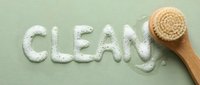 Wooden brush with natural bristles and scattered powder forming the word clean on soft green background, representing hygiene and cleaning products.