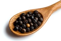 Black peppercorns in wooden spoon on white background, aromatic whole spices for cooking and seasoning, isolated macro food photography.