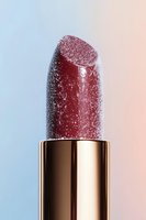 Sparkling red lipstick with water droplets on rose gold tube against soft gradient background for beauty and cosmetics advertising campaigns.
