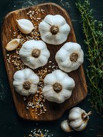 Fresh whole garlic bulbs and cloves arranged on rustic wooden cutting board with herbs and sea salt, dark moody background for food photography and cooking blogs.
