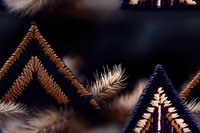 Decorative chevron pattern embroidered in metallic copper and navy blue threads on dark fabric, with delicate feather-like stitching details creating texture and depth.