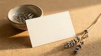 Blank white card leaning against ceramic bowl with dried lavender flowers and loose tea leaves on natural beige textured surface for wellness, spa, herbal product marketing.