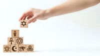 Hand placing Star of David wooden block completing pyramid of religious symbols representing interfaith unity and spiritual diversity.