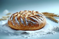 Fresh baked round bread loaf with crispy golden crust and diagonal cuts on white parchment paper, dusted with flour, wheat ears decoration.