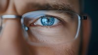 Close-up view of bright blue eye seen through modern eyeglasses frame, showing detailed iris texture and reflection in lens, highlighting vision and optical care.