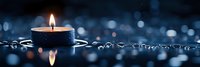 Burning candle with reflection on dark blue background with water drops and bokeh lights creating peaceful atmospheric mood for spa and relaxation.