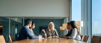 Senior businesswoman leading team meeting in modern conference room with diverse colleagues discussing strategy and collaboration.