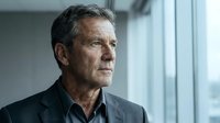 Senior man with gray hair and weathered features wearing dark casual shirt, looking thoughtfully to the side near bright window. Suitable for corporate, healthcare, and lifestyle editorial use.