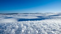 Aerial view of vast snowy landscape with rolling white hills and clear blue sky, suitable for winter travel, nature, and environmental design projects.