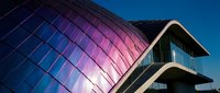 Modern curved glass building facade with iridescent purple and blue panels against clear sky, contemporary architecture design for commercial, corporate, or tech industry projects.